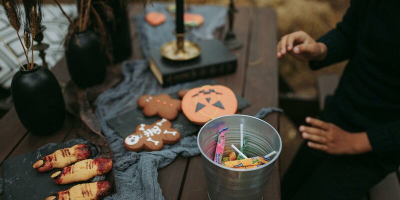 a person sitting at a table with halloween decorations and a bucket of candies